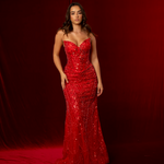 Woman in a red sequin gown standing against a red curtain.