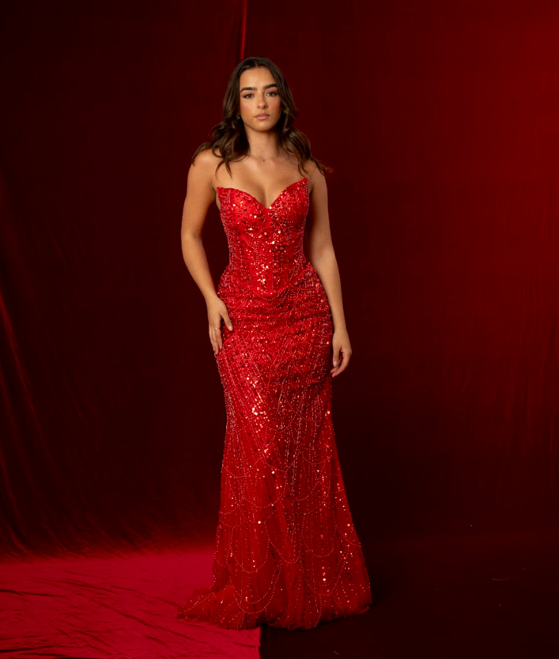 Woman in a red sequin gown standing against a red curtain.