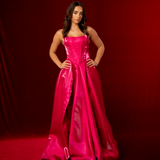 A hot pink satin formal gown with a straight neckline, basque waist, corset back, and thigh-high slit.
