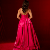 A hot pink satin formal gown with a straight neckline, basque waist, corset back, and thigh-high slit.