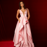 A baby pink formal A-line gown with plunging V neckline, thick straps, corset back, and dramatic liquid taffeta ruffled skirt.