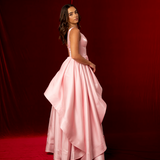A baby pink formal A-line gown with plunging V neckline, thick straps, corset back, and dramatic liquid taffeta ruffled skirt.